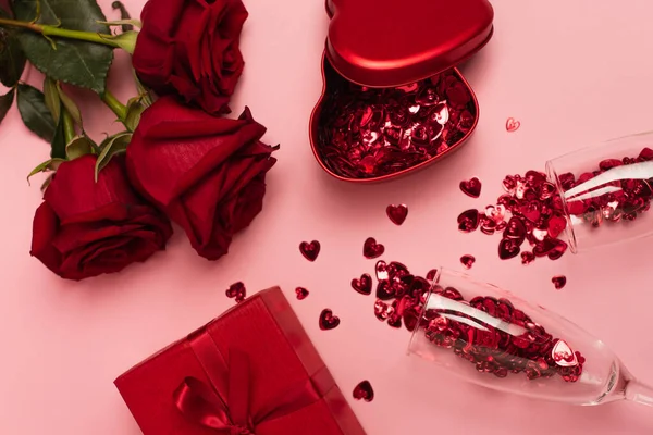 Ansicht von Champagnergläsern mit Konfetti-Herzen in der Nähe von Geschenkboxen und Rosen auf rosa — Stockfoto