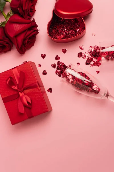 Top view of champagne glasses with confetti hearts near gift boxes and red roses on pink — Fotografia de Stock