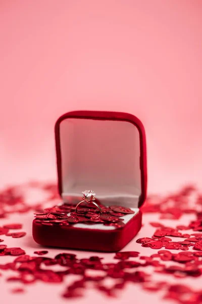 Close up of jewelry box with diamond ring near shiny confetti hearts on pink — Foto stock