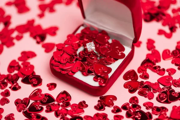 Close up of jewelry box with diamond ring near red confetti hearts on pink — Foto stock