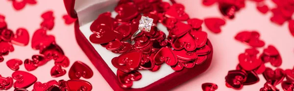 Close up of jewelry box with diamond ring near red confetti hearts on pink, banner — Stock Photo