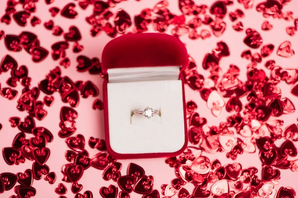 Vue du haut de la boîte à bijoux avec bague en diamant près des cœurs de confettis brillants sur rose — Photo de stock