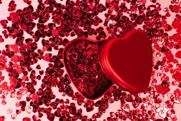 Top view of metallic heart-shaped box near shiny red confetti hearts on pink — Stockfoto