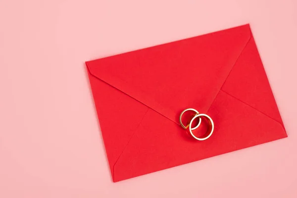 Vue de dessus des anneaux sur enveloppe rouge isolé sur rose — Photo de stock