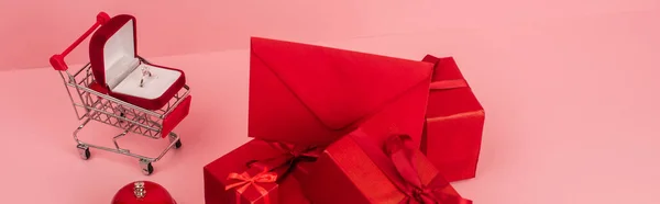 Красные упакованные подарочные коробки и конверт рядом с корзиной с обручальным кольцом на розовом, баннер — стоковое фото