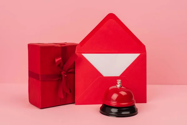 Geschenkverpackung und roter Umschlag mit Brief in der Nähe einer metallischen Glocke auf rosa — Stockfoto