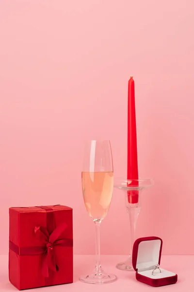 Coupe de champagne près boîte cadeau, bague de fiançailles et bougie sur rose — Photo de stock