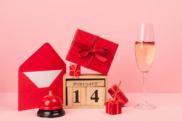 Caixas de presente vermelho no calendário de madeira com 14 fevereiro lettering perto do envelope, champanhe em vidro e sino no rosa — Fotografia de Stock