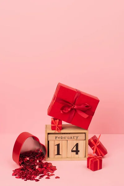 Coffrets cadeaux rouges près du calendrier en bois avec lettrage 14 février près de confettis sur rose — Photo de stock