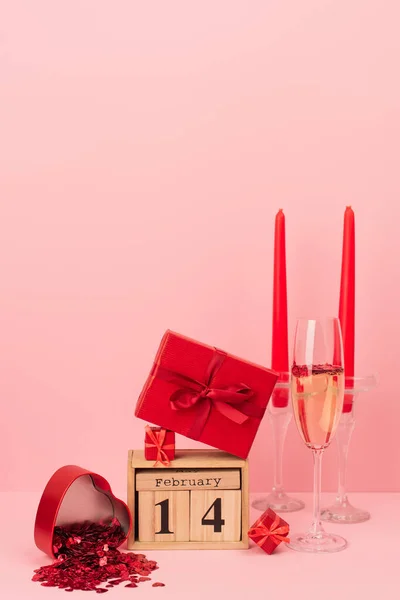 Coffrets cadeaux rouges sur calendrier avec lettrage 14 février près de champagne en verre, bougies et confettis sur rose — Photo de stock
