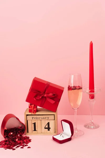 Caixas de presente vermelho no calendário com 14 fevereiro perto de champanhe em vidro, anel de noivado, vela e confete em rosa — Fotografia de Stock