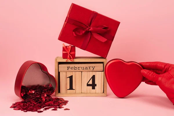 Cropped view of woman holding heart-shaped metallic box near presents and calendar on pink — Stock Photo