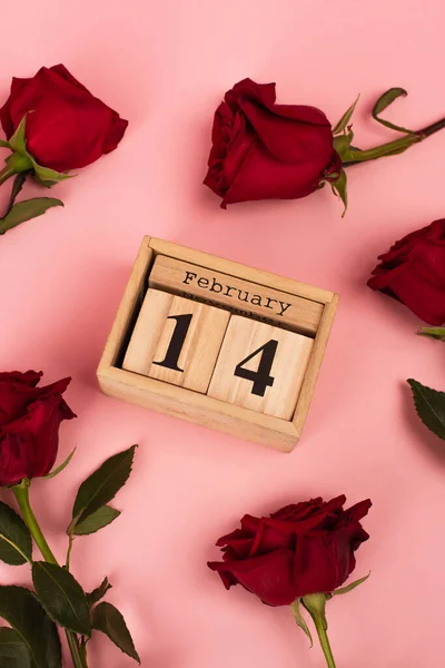 Top view of red roses near wooden calendar with 14 february lettering on pink — Fotografia de Stock