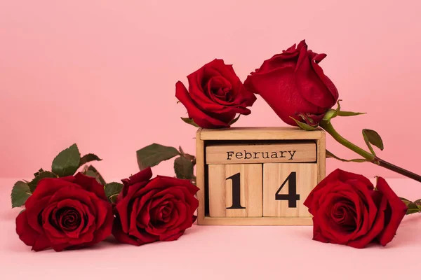 Red roses near wooden calendar with 14 february lettering on pink — Fotografia de Stock