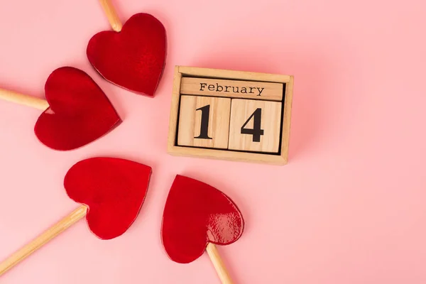 Leigos planos de pirulitos em forma de coração perto do calendário de madeira com 14 de fevereiro no rosa — Fotografia de Stock