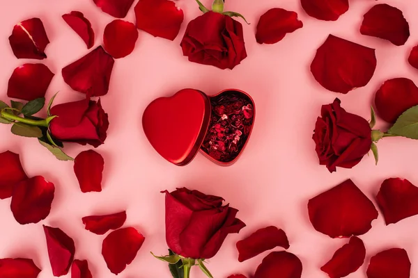 Flat lay of red rose petals around metallic box with confetti on pink — Foto stock