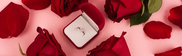 Flat lay of red rose petals around jewelry box with diamond ring on pink, banner — Stock Photo