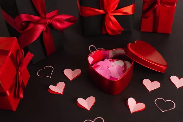 Papiergeschnittene Herzen in der Nähe von Metallschachteln und verpackte Geschenke auf Schwarz — Stockfoto
