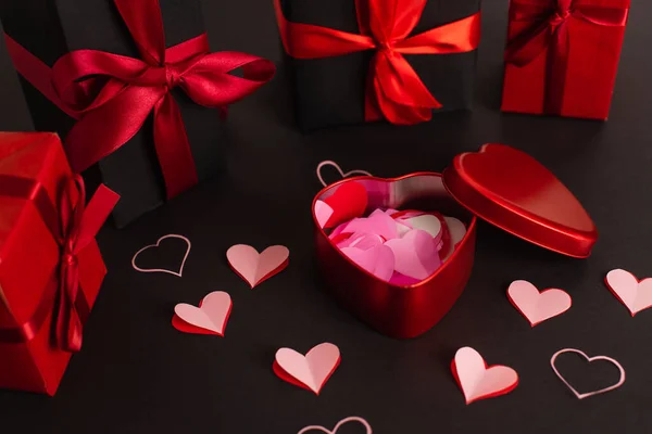 Corazones cortados de papel cerca de caja metálica y regalos envueltos en negro - foto de stock