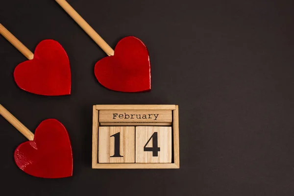 Top view of wooden calendar with 14 february lettering near heart-shaped lollipops on black — Stock Photo