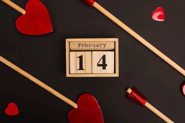 Vista superior del calendario de madera con 14 febrero cerca de piruletas en forma de corazón en negro — Stock Photo