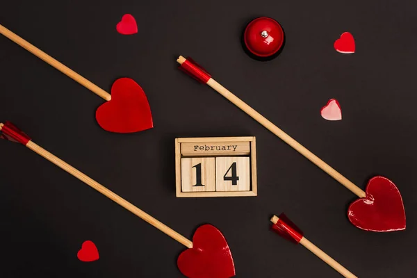 Top view of wooden calendar with 14 february lettering near red heart-shaped lollipops on black — Stock Photo