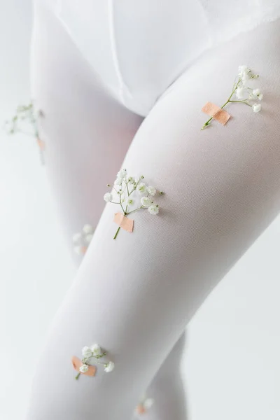 Vista ritagliata della donna in calzamaglia decorata con fiori di gypsophila isolati su grigio chiaro — Foto stock