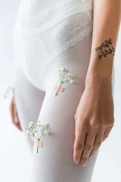 Partial view of tattooed woman with gypsophila flowers on tights isolated on light grey — Stock Photo