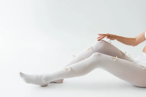 Cropped view of woman wearing tights with tiny gypsophila flowers sitting on light grey background — Stock Photo