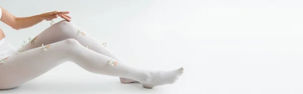 Cropped view of woman with tiny flowers on tights sitting on light grey background, banner — Stock Photo