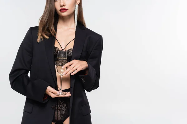 Vista ritagliata di donna sexy in blazer nero e lingerie di pizzo in posa con bicchiere di champagne su grigio — Foto stock