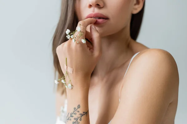 Vista recortada de mujer joven con flores minúsculas en mano tatuada aislada en gris - foto de stock