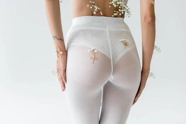 Vue partielle de femme sexy avec de petites fleurs sur le corps debout en culotte blanche et collants isolés sur gris — Photo de stock