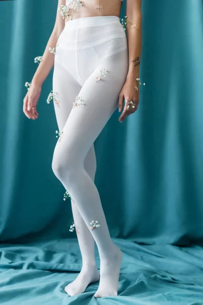 Visão parcial de mulher tatuada com flores minúsculas em meias de pé sobre cortinas verdes — Fotografia de Stock