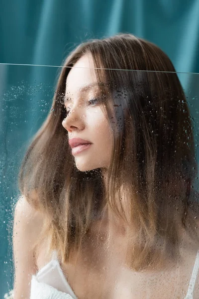 Sensual brunette woman near wet glass and turquoise drape on background — Stock Photo