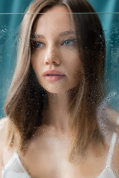 Close up view of young brunette woman posing near wet glass on turquoise background — Stock Photo