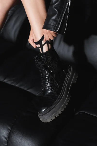Vista cortada da mulher na bota de couro preto ajustando meia perto do sofá — Fotografia de Stock