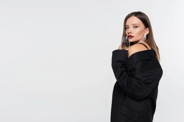 Jeune femme sensuelle en blazer noir tenant verre de champagne tout en regardant la caméra isolée sur gris — Photo de stock