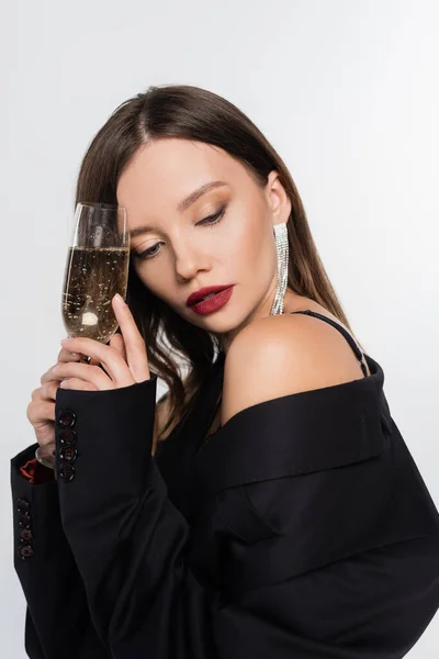Seductive brunette woman in black blazer holding glass of champagne isolated on grey — Stock Photo
