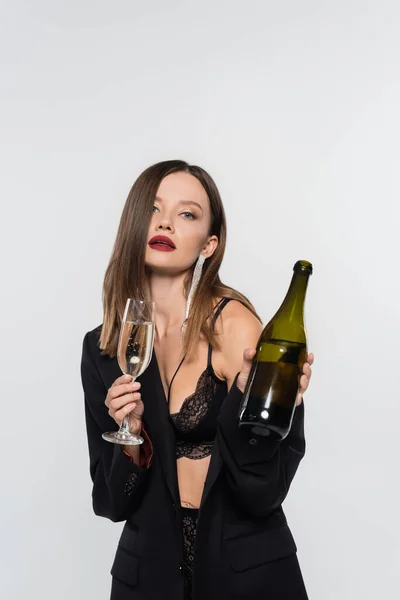 Сексуальна жінка в нижній білизні і чорний блейзер тримає скло і пляшку шампанського ізольовані на сірому — стокове фото