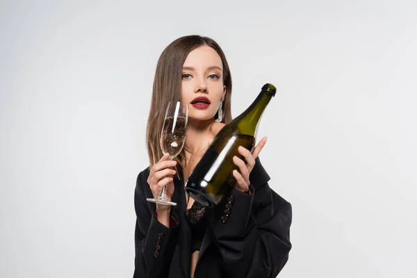 Seducente bruna donna in blazer nero in posa con bottiglia e bicchiere di champagne isolato su grigio — Foto stock