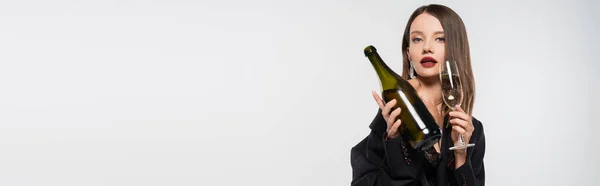 Sinnliche Frau im schwarzen Blazer mit Flasche und Glas Champagner in der Hand, während sie isoliert in die Kamera auf grau blickt, Banner — Stockfoto