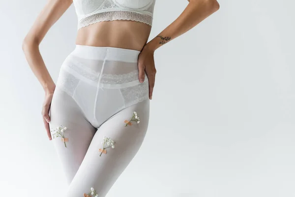 Vue recadrée de femme mince en soutien-gorge blanc, culotte et collants avec des fleurs de gypsophila posant isolé sur gris — Photo de stock