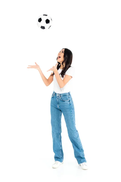 Vue pleine longueur de femme excitée en jeans jouant avec le ballon de football sur blanc — Photo de stock