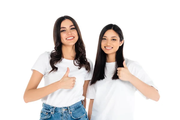 Young brunette multiethnic women showing thumbs up while smiling at camera isolated on white — стоковое фото