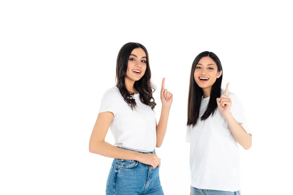 Joyful multiethnic women looking at camera and pointing with fingers isolated on white — стоковое фото