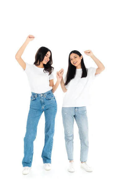 Vista completa de mujeres multiétnicas felices en camisetas y pantalones vaqueros bailando en blanco - foto de stock