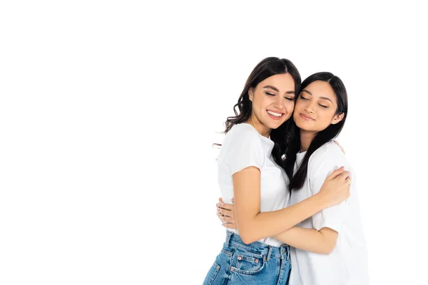 Pleased interracial women in t-shirts embracing with closed eyes isolated on white — Stock Photo