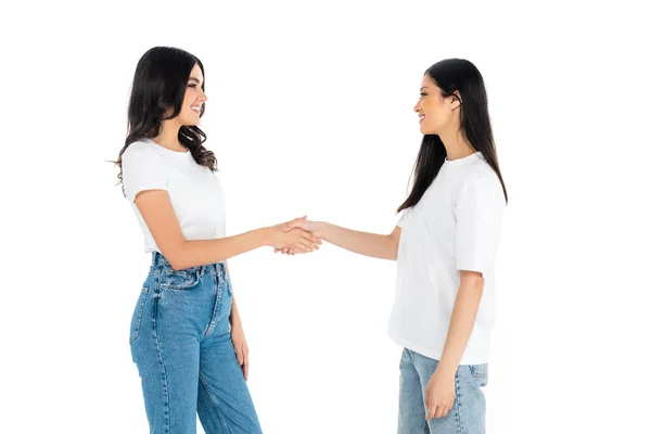 Happy brunette multiethnic women looking at each other and shaking hands isolated on white — стоковое фото