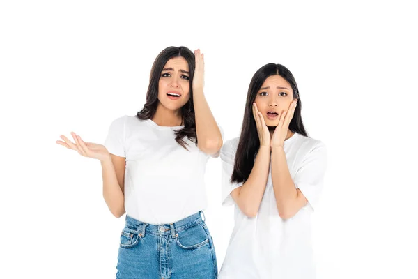 Upset woman pointing with hand near shocked asian friend touching face isolated on white — Foto stock